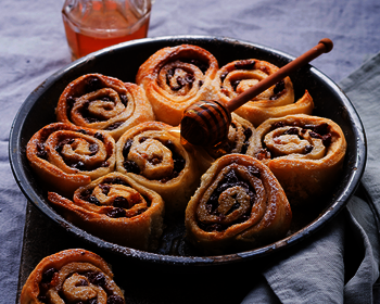 Picture of bejgli dough swirls, prepared of Wewalka bejgli dough, being presented in a pan on a kitchen table, being topped with honey